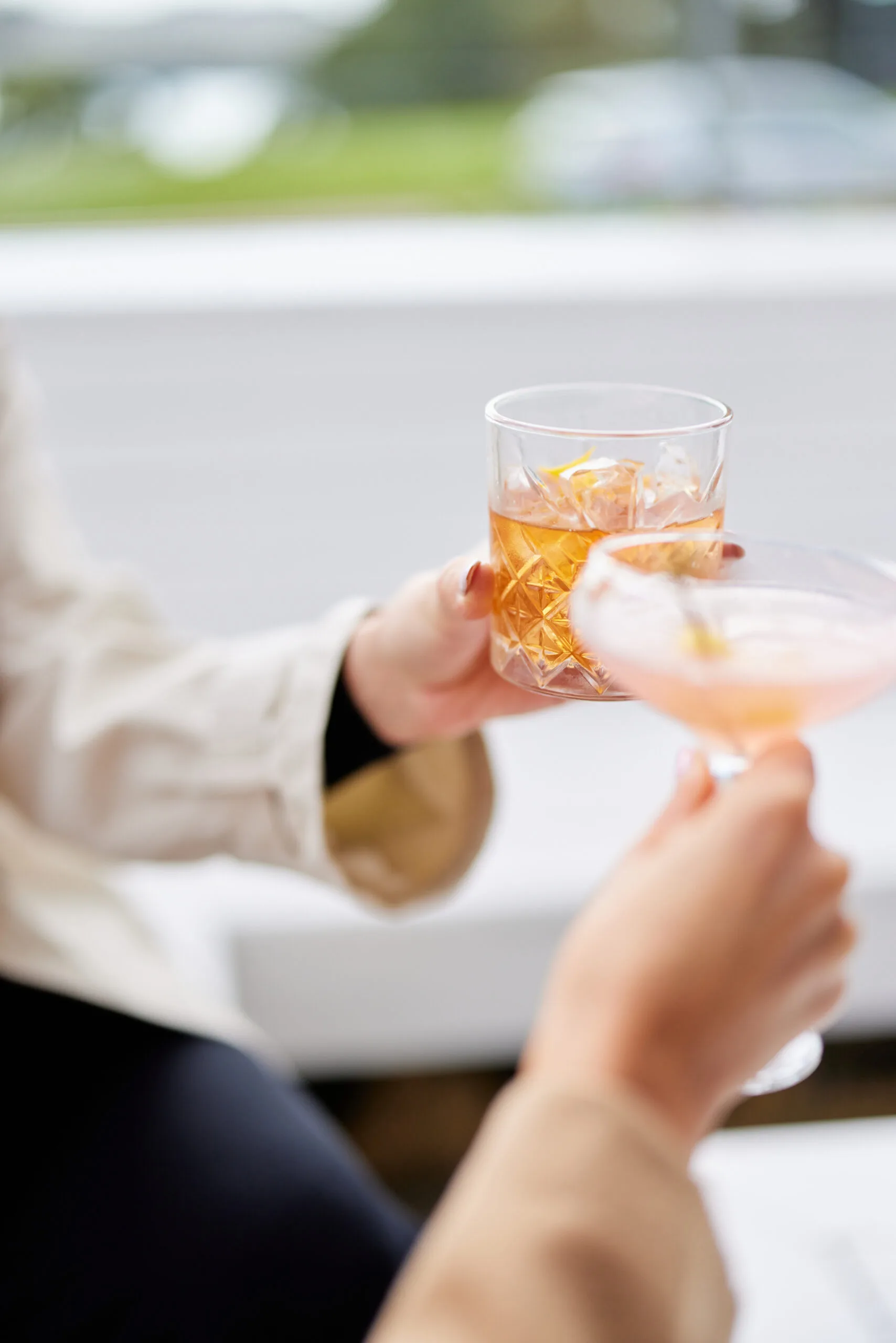 Two people clinking glasses of cocktails, one with ice and a lemon twist.